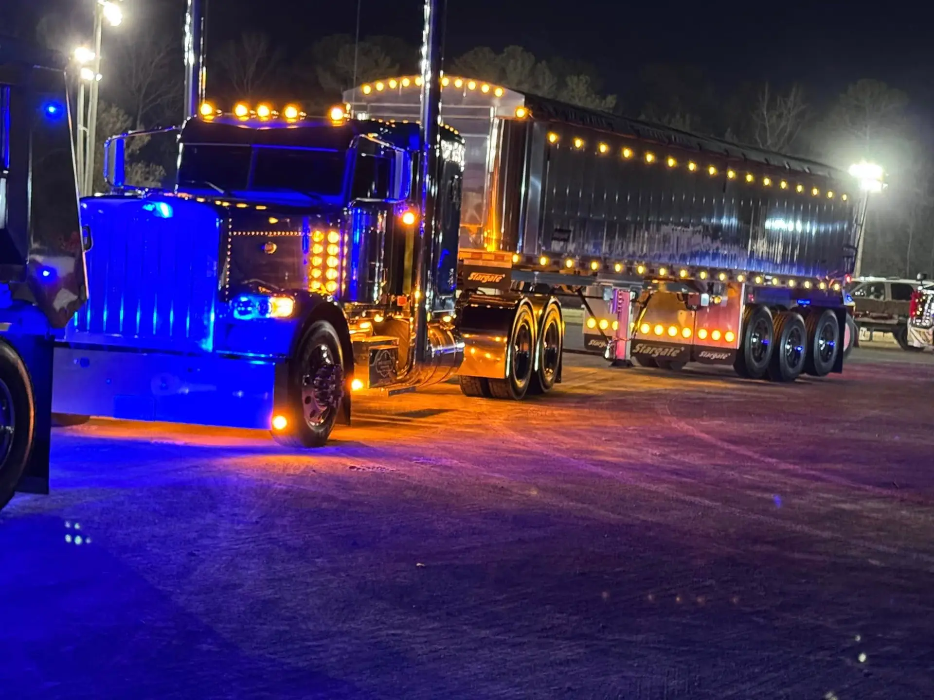 Line of lit-up Bunn family dump trucks with blue and amber lights at night